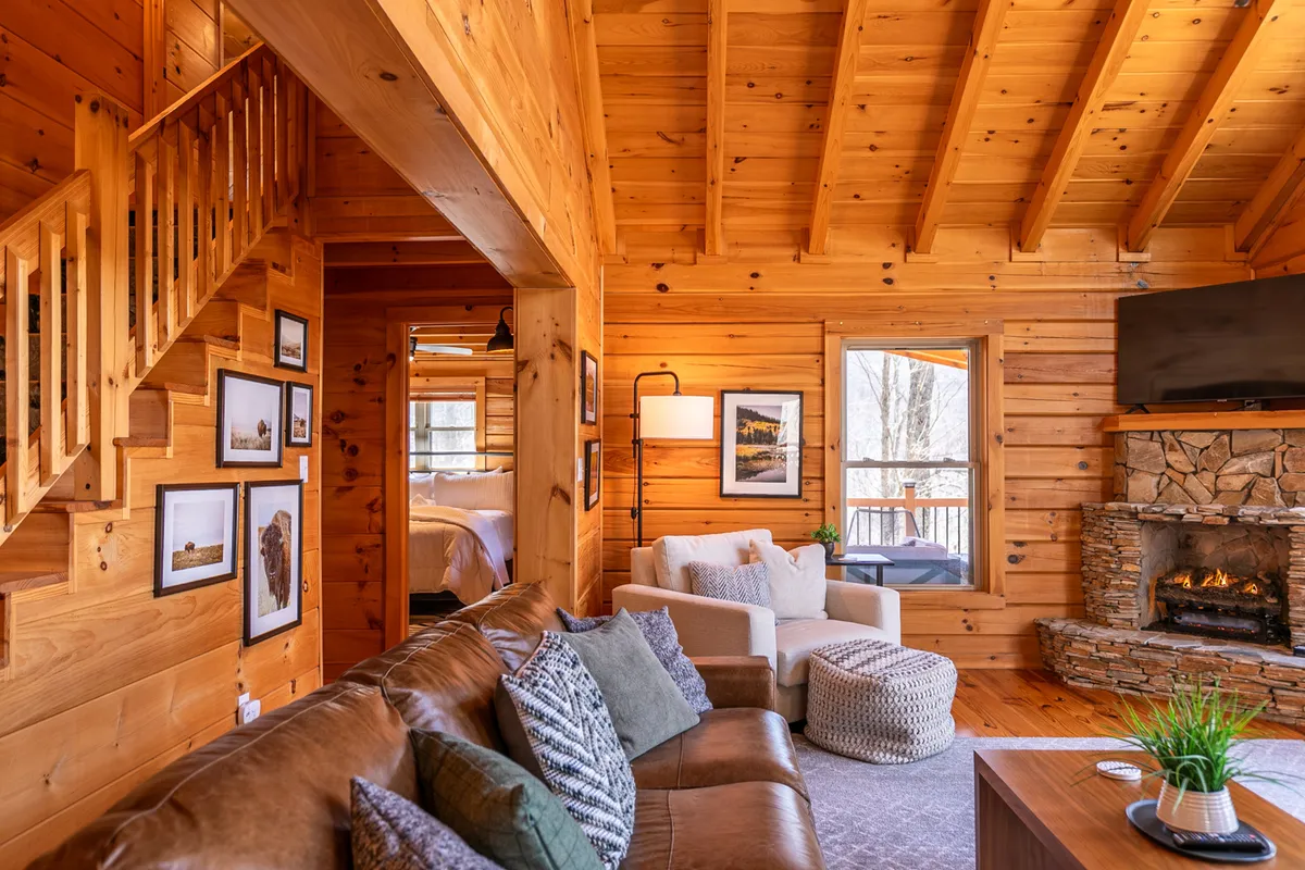 A cozy living room with a prominent stone fireplace, comfortable sofa, and expansive windows that look out onto the surrounding natural landscape. Artwork decorates the walls, and the overall ambiance is warm and inviting, suggesting an ideal spot for couples to unwind after a day of exploration.