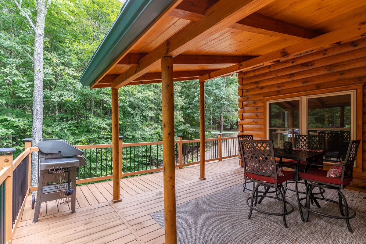 This image showcases an inviting outdoor dining set complete with a grill, nestled on the deck and surrounded by forest. The setting is tranquil and immersed in nature, creating a perfect spot for unwinding after a day of outdoor adventures. The deck’s proximity to the trees and the open sky enhances the feeling of escaping into the mountains.