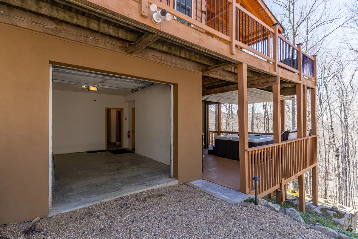 This exterior shot showcases the hot tub area on the wooden deck, adjacent to the garage entrance. The spacious deck offers plenty of room for guests to relax and socialize while enjoying the scenic mountain air.