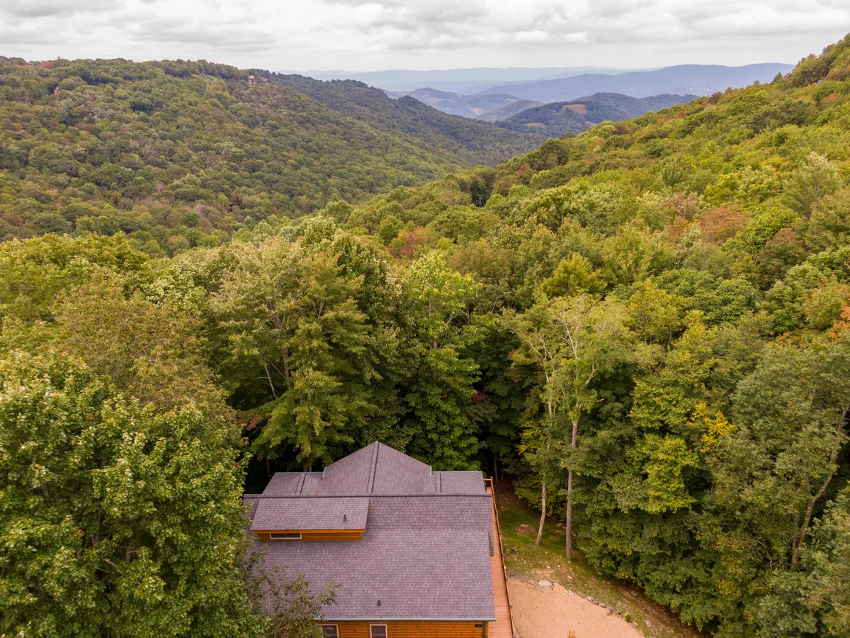 This image shows the lodge nestled among tall trees with an expansive mountain view in the background. The gravel path leads up to the house, emphasizing its secluded location and proximity to nature. The setting captures the peacefulness and majesty of the surrounding landscape, ideal for outdoor adventures like hiking and wildlife observation.