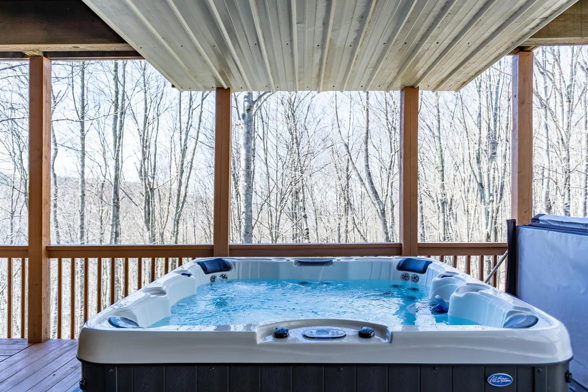 This image showcases a private hot tub nestled within a wooden structure, surrounded by lush mountain nature. The setup evokes relaxation with the promise of serene stargazing or morning coffee while taking in the natural views, and the atmosphere is tranquil and inviting.