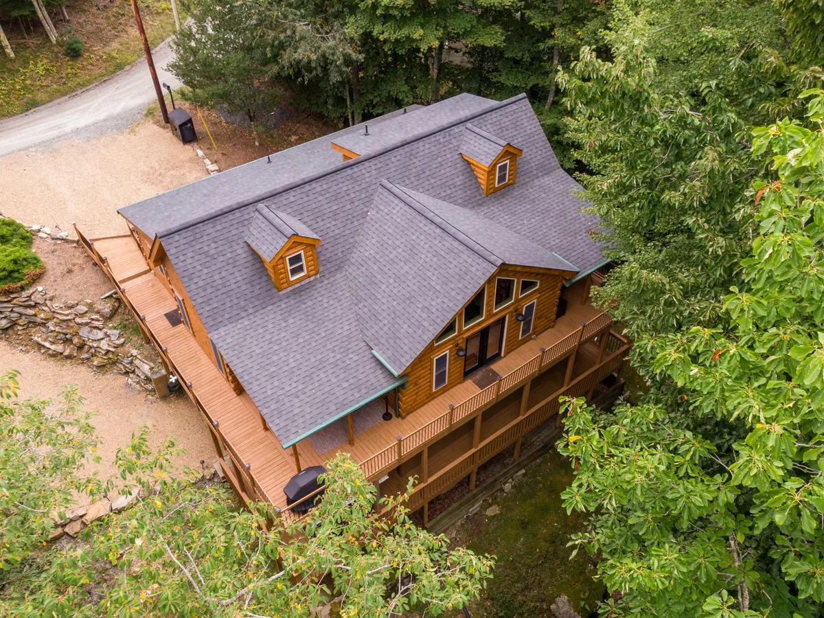 This image presents the wide wooden deck with views of the large cabin windows and the surrounding trees. It conveys a welcoming space where families and groups can gather for outdoor meals, conversations, or simply enjoy the peaceful ambiance.