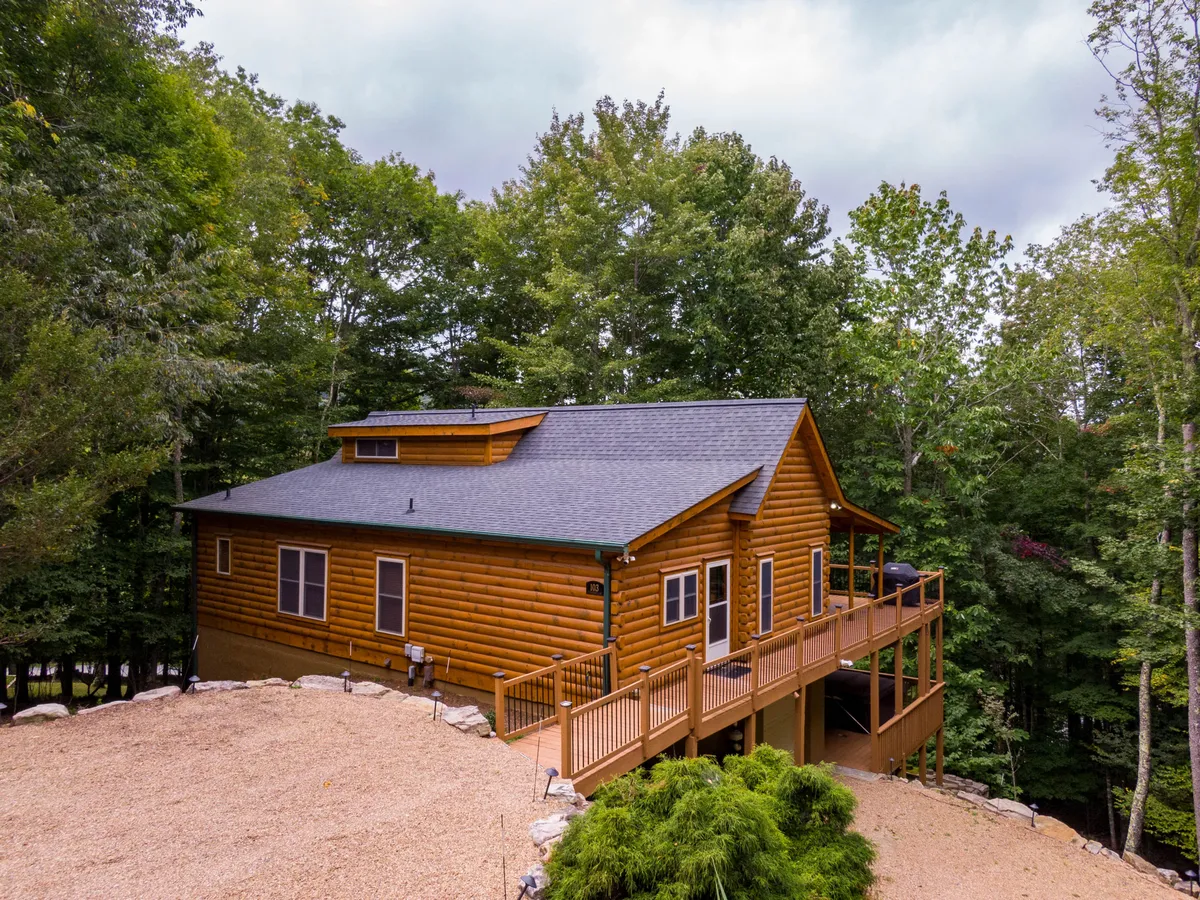This image features the log cabin structure of the lodge, its spacious deck, and mature trees encircling the property. The setting is tranquil and inviting, ideal for relaxing after a day of mountain sports or evening stargazing.