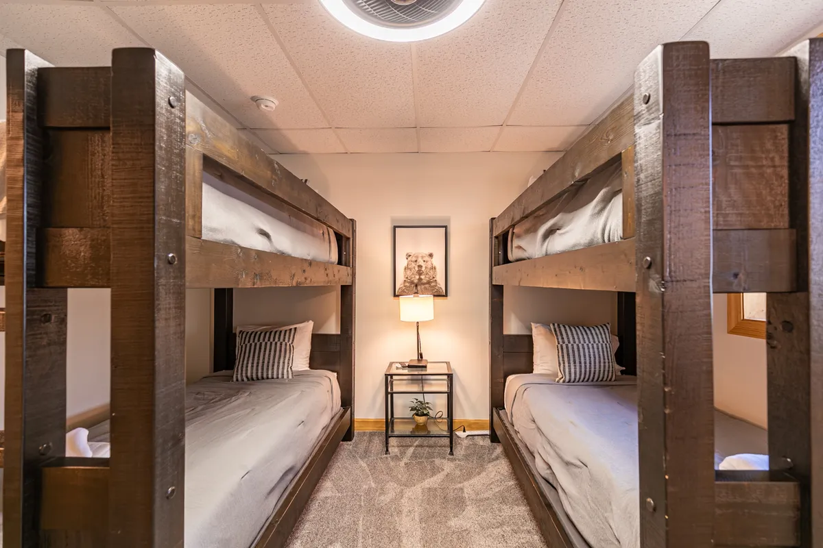 A lively bunk room with sturdy bunk beds, a cheerful table lamp, and framed artwork, creating a fun and welcoming hideaway for kids or teens. The space is bright and designed for both sleep and play.